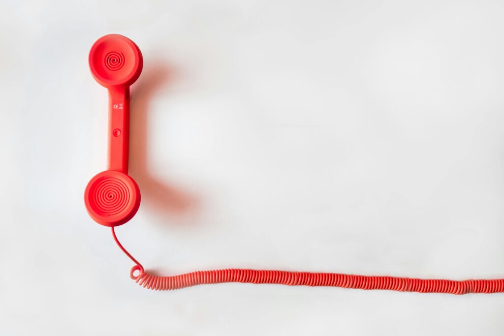 Vintage red phone handset with coiled cable on a clean white background, classic communication device.